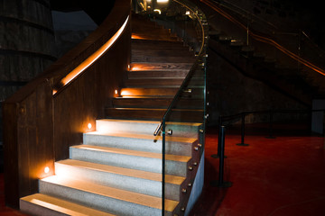 Stairs with glass fence under artificial light. The staircase is located in a dark basement.