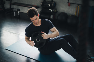 Young man caucasian was exercising by the use weight plate on yoga mat. He wears sportswear....
