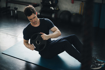 Young man caucasian was exercising by the use weight plate on yoga mat. He wears sportswear. Fitness in the gym concept.