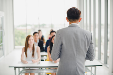 Asian male speaker is speaking at seminars and workshops to the people in the meeting. Participants are raising their hands to ask questions.