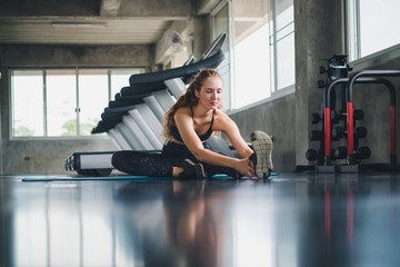 Beautiful athlete put on a sports suit. Stretching a muscle on a yoga mat. Before playing sports in the gym. She is relaxing