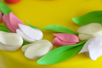 Top decoration of cake with tulip flower made from mastic on yellow background, spring mood