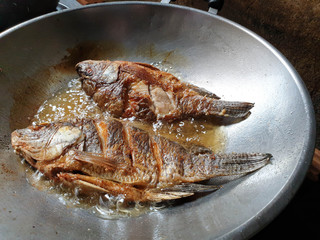 Closeup of Thai tradition and local food "Fried tilapia with salt" frying on Chinese pan.