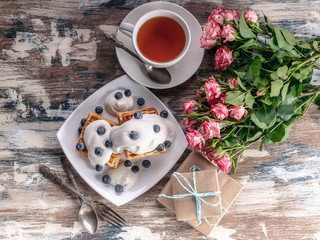 Women's day concept. Belgian waffles with blueberries, gift boxes and roses, a cup of tea. Top view