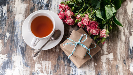 Bouquet of roses, gifts and tea on a wooden rustic background. Women's day concept. Top view