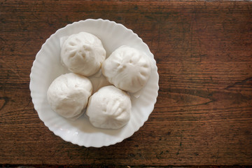 Top view Chinese hot bun on white ceramic plate and wooden table background. Chinese hot bun or SALABAO are various types (pork, bean, custard) Popular in winter in China, Hong Kong, Taiwan.