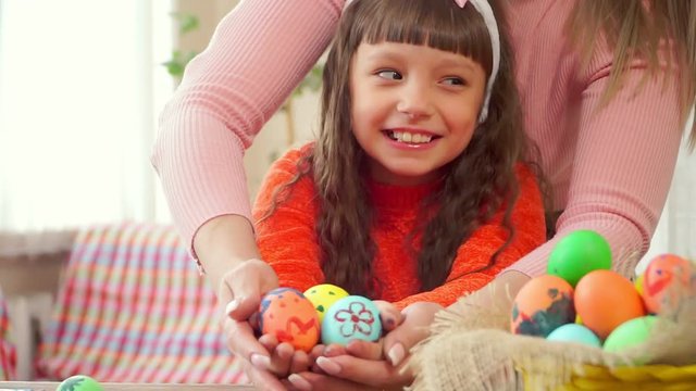 Portrait of cheerful little kid girl playing together with his mother with easter egg on the kitchen background. holding Easter eggs