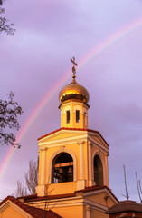 The golden domes of the Orthodox Christian church in the rays of the evening sun setting against the background of a bright multi-colored rainbow after the rain. Rainbow, Good News, Gospel