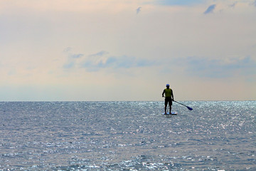 Silhouette of active surfer on stand up paddle board paddling in sea