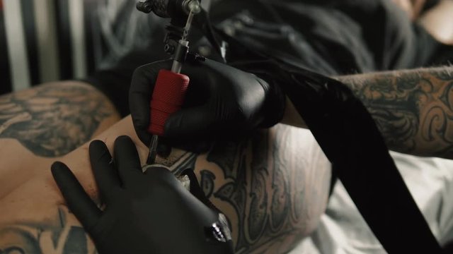 Close up macro tattoo male artist makes a tattoo on a female leg, professional man with machine gun paint draw