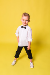 Fashionable cute adorable caucasian boy model posing on yellow background. Fashion kids, childhood, beauty concept