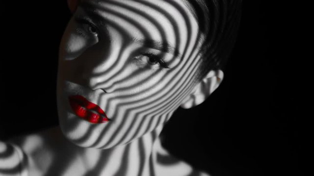 Projection of black and white lines on girl&rsquo;s face. Close up eyes of girl with an abstract pattern of lines and red lips on her face. Illumination from the blinds in the room. Concept. Sharp look.