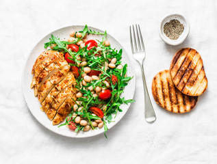 Delicious healthy lunch - baked chicken breast and white beans, arugula, cherry tomatoes salad on a light background, top view