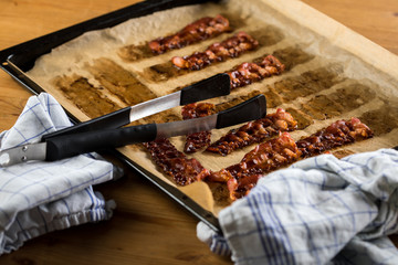 Knusprig gebratene Bacon Speck Scheiben aus dem Ofen auf Backblech mit Backpapier mit Geschirrtuch...