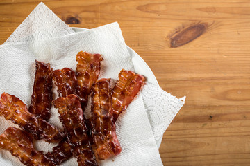 Knusprig gebratene Bacon Speck Scheiben auf Teller zum Fett abtropfen mit K&uuml;chenkrepp auf Holz Tisch Hintergrund