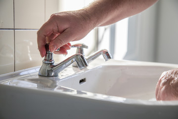 Mann nutzt Waschbecken mit Leitungswasser zum Händewaschen