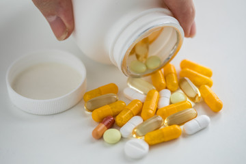 Frau nimmt Pillendose mit gelben und weißen Pillen Kapseln und Tabletten auf weißen Hintergrund