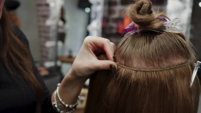 The hairdresser sews artificial hair to the real thing. The process of hair extension. 4K