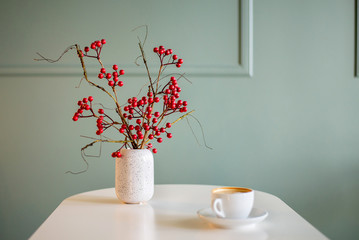 a bouquet of berries on the table in a vase and a cup of coffee