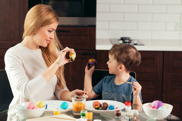 Little boy and his young blonde mom showing to each other colorful self-painted Easter eggs. Family celebration and home decoration for spring holiday.