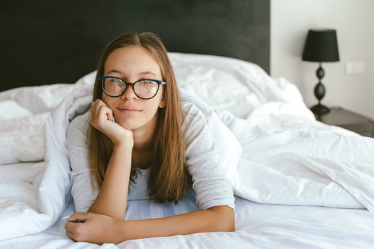 Portrait of a 12-13-14 years old teenage girl wearing eyeglasses in bed