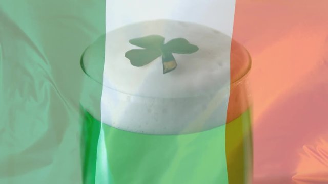 Shamrock falling on a green beer against an Irish flag background for St Patrick Day