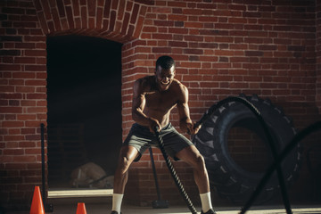 Fototapeta na wymiar Afro american bodybuilder with battle rope in cross-fit training centre
