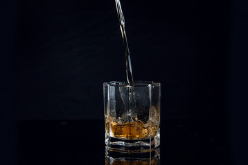 Whiskey pouring into glass with ice isolated on black background..