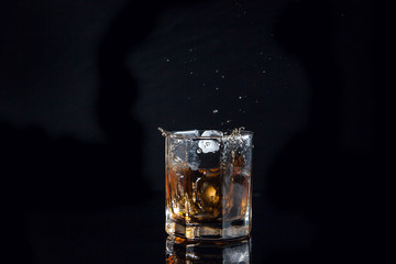 Whiskey splash from the fallen ice cube into glass with beverage isolated on black background..