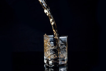 Whiskey pouring into glass with ice isolated on black background..