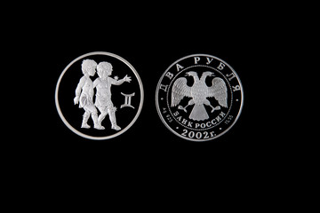 Silver coin of the Bank of Russia with the sign of the zodiac Gemini on a black isolated background. The coin says: "Two rubles. Bank of Russia".