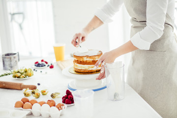 woman appling buttercream between layers, close up cropped photo. girl putting a huge amount of icing on the top of the cake