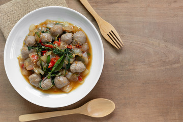 top view of stir fried meatball with basil in a ceramic dish on wooden table. hot and spicy thai style food menu.