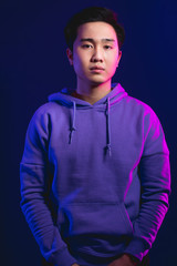 Obraz premium Portrait of a handsome young Japanese man, dressed in casual wear. Not emotional guy looking at camera with serious face, isolated at studio against puple wall