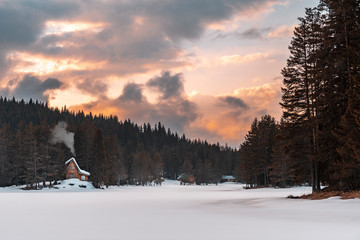 Small mountain house in the forest. Frozen lake in front. Winter landscape.