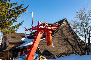 The mechanism of the ski lift, visible large, driving wheel pulling a rope in the background of an old house.