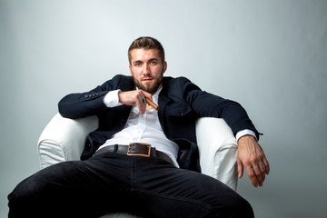 Portrait of a bearded businessman with a cigar, who is sitting in a white armchair and relaxing