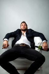 Portrait of a bearded businessman with a cigar, who is sitting in a white armchair and relaxing