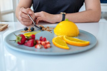 A woman eating orange cake with mixed fruit by spoon in cafe