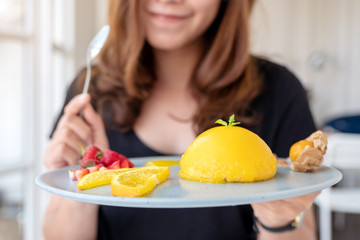 A beautiful asian woman holding a plate of orange cake with mixed fruit and a spoon in cafe