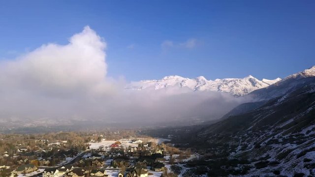 View of houses below the clouds on a blue bird day in Utah panning towards the mountains.
