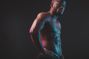 Attractive African male fighter or boxer posing shirtless, looking at camera, isolated over dark background. Awesome young bodybuilder.