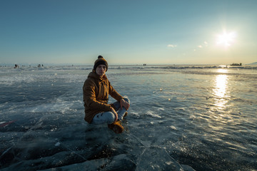 Fototapeta premium Tourist with a backpack meditates sitting in Lotus position on the ice of lake Baikal. Calm and freedom of nature