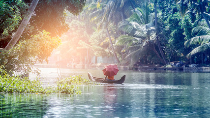 A man with an umbrella in a traditional boat sails through the backwaters of Alleppey in Kerala, South India. ALAPPUZHA KERALA - obrazy, fototapety, plakaty
