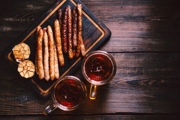 beer and appetizing snacks. table with two mugs of craft lager, wooden board with homemade grilled sausages, garlic and sauce, salted nuts. oktoberfest food, pub concept