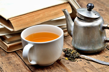 Detail of old books, mug of black tea, old teapot and spoon with tea loose