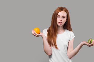 serious slim girl in white T-shirt holding an orange and apple.diet concept, body care. woman leads healthy lifestyle