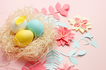 Coloeful easter eggs in nest on pastel color background with origami papercraft flower decoration. Copy space, greeting card