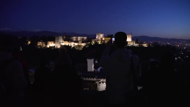 Silhouette of tourists taking photos of the Alhambra after the sunset.