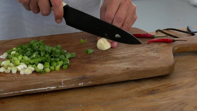 Slicing a glove of garlic among celery and chillies on a cutting board